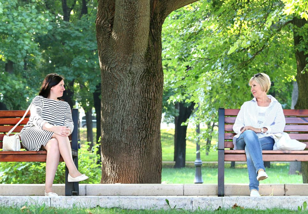 Zwei Frauen sitzen jede alleine auf einem Sitzbank im Park und schauen sich an