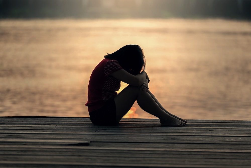 Silhouette einer Frau an einer Seebrücke die sich verzweifelt an Ihre Beine lehnt